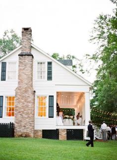 white farmhouse with brick chimney, black shutters, and of course a big porch.