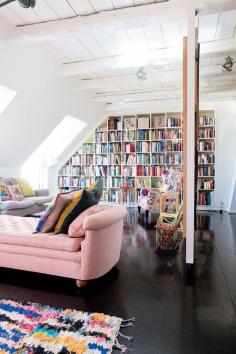 pink couch, dark floors, white walls, wall to wall bookcase, slanted ceilings/attic // living room, library
