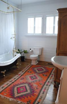 White bathroom, wood floor, Aztec tribal rug, clawfoot tub and brass fixtures