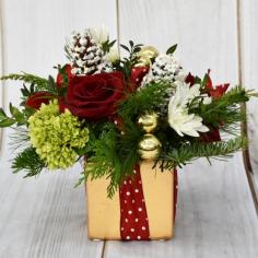 CHERISH THIS TIME OF YEAR WITH BEAUTIFUL FLOWERS TOPPED WITH A BOW IN THIS BOX ARRANGEMENT FEATURING CHRISTMAS GREENS, SHORT STEM ROSES AND MINI GREEN HYDRANGEA

