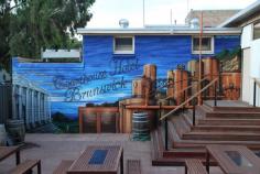 Exterior Beer Garden Mural Painted at 615 Sydney Rd. Melbourne. Courthouse Hotel Brunswick. The combination of elements included in this painting: Title of the venue in a scripted typeface. Sky Blue backdrop to keep the beer garden main colours to a cooling vibe. A painted brewery to tie in comfortably with all the pipes that are currently fixated on the wall. This also hides and uses the real pipes as part of the mural. The courthouse painted on the left side as the title of the business is directly correlated.