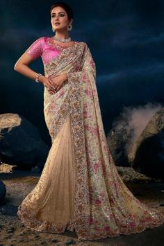 The cream Indian sari is crafted in premium net fabric and is decorated with eye-catching applique floral work done with Resham, sparkly sequins, shiny stones, pearls, and handmade 3D flowers, along with a graceful printed pallu. This beautiful drape is paired with a pink embellished silk blouse.