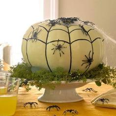 Paint an artificial pumpkin with white acrylic paint; let dry. Use a black paint pen to draw on a web: first draw the vertical lines (follow the veins of the pumpkin), then draw scalloped horizontal lines as shown. Adhere spider webbing to the top of the pumpkin and plastic spiders to the sides using crafts glue. Place the finished pumpkin on a cake pedestal and surround with greenery.