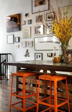Kitchen Island with industrial Stools painted orange. Gallery Art wall in the background.