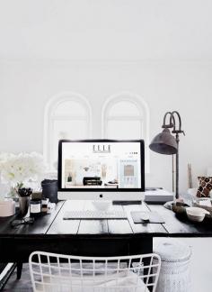 Clean black and white office with wire chair and desk lamp.