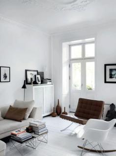 living room white décor magazine stacks neutral picture frames window white walls and flooring