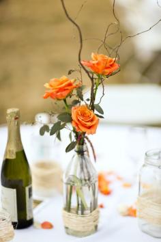 Understated centerpieces for a casual gathering.... ie: Old bottles, then the  bottom wrapped in twine or string or raffia, & then 3 open roses in the bottles, with tiny branches and leaves.