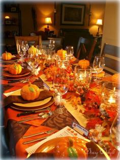 Dining Delight: Fall Dinner Party for Ten. Orange brown yellow. 5 double wall hurricane vase centerpiece. Outside filled with river rocks, inside with orange gems, water, floating candles. Place setting: gold charger, orange plate, pumpkin tureen. Looks like placemat is orange napkin turned in diamond shape.
