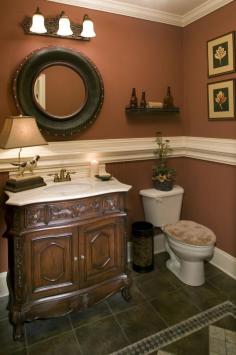 Very traditional bathroom with an ornate dark wood vanity, red painted walls, off white painted millwork and dark tile floor. Could use some light.