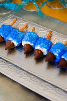 
                    
                        Hanukkah dreidel dessert-  Using a thin layer of white frosting, coat all surfaces of the marshmallow. Then break a thin pretzel rod in half and dip the end into the white frosting. Stick that end into the flat side of the marshmallow to create the handle for the dreidel. Holding the pretzel stick, roll the marshmallow in the sprinkles until its fully covered. Apply a small dab of white frosting to the Hershey Kiss and affix to the other flat side of the marshmallow to create the ‘spinner'.
                    
                