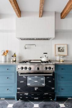 Blue cabinetry in white kitchen with exposed ceiling beams and white teapot