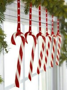 Candy canes make vibrant eye-catching window ornaments. Hang a series of candy canes with colorful ribbon from the curtain rod. An evergreen garland draped along the top of the curtain rod adds the finishing touch! ~ Christmas Window Decorations | Christmas Window Decorating Ideas