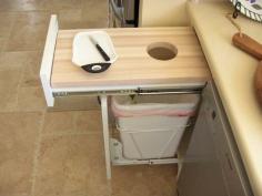 A smart idea that need not have an official trash bin drawer (though that is handy if you are redoing your cabinets anyway.)  Set up a sturdy drawer with a carefully sized cutting board (make sure it is secured to avoid accidents.)  Place your compost bin or trash basket underneath the cutout--even a short drawer below would work for a compost bowl or bucket and then both can be easily closed.