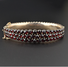 This antique Victorian three-row bangle bracelet is graced with rich pomegranate red rose cut Bohemian garnets. The garnets are set in a pinchbeck gold frame giving the border a scallop design. Expertly crafted, the hinged bangle bracelet is closed with a tongue slide clasp and safety chain. Stack with others or wear alone.